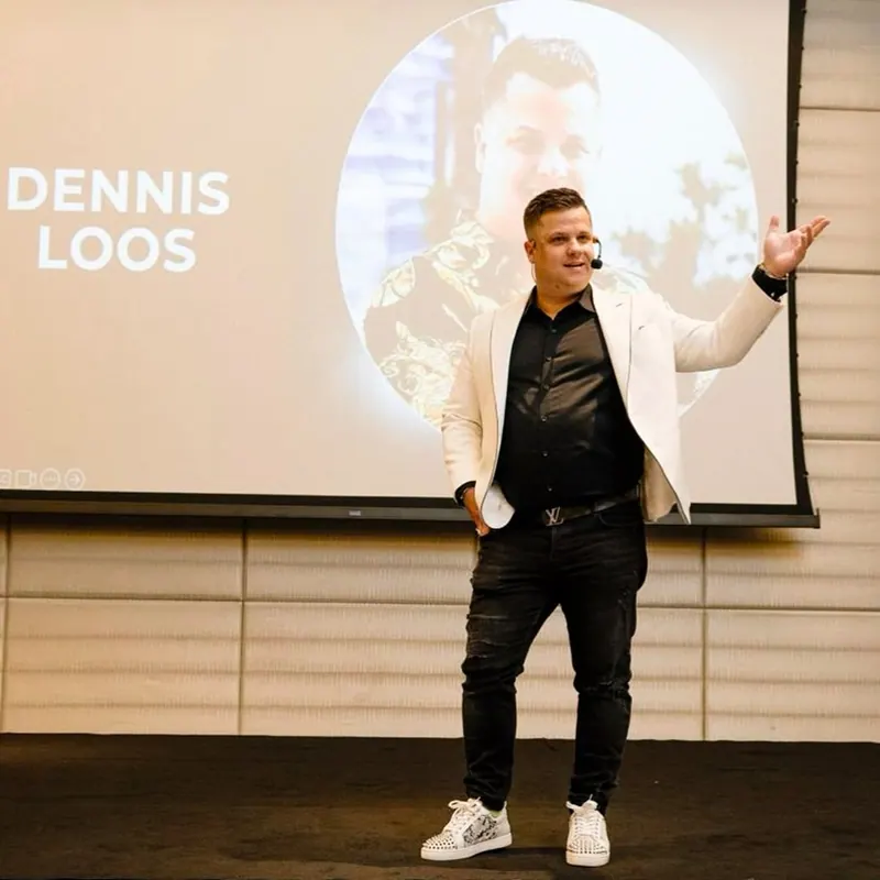 Dennis Loos als Speaker auf der Bühne, hinter ihm sein eigenes Porträt auf der Leinwand