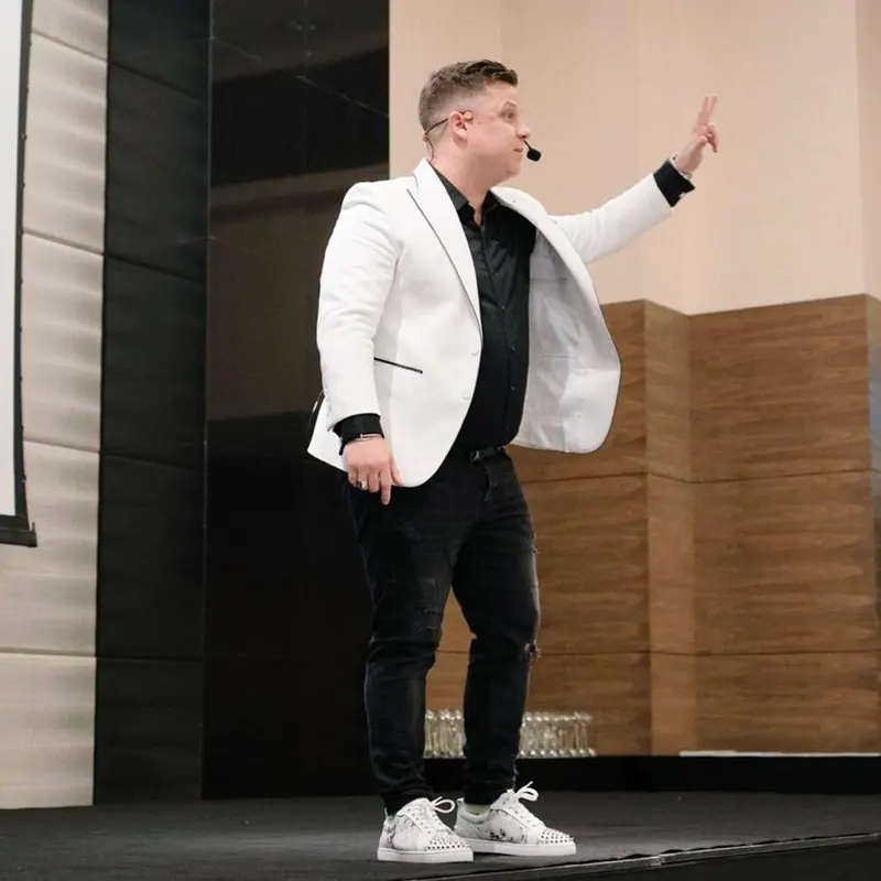 Dennis Loos im weißen Blazer auf der Bühne, winkend